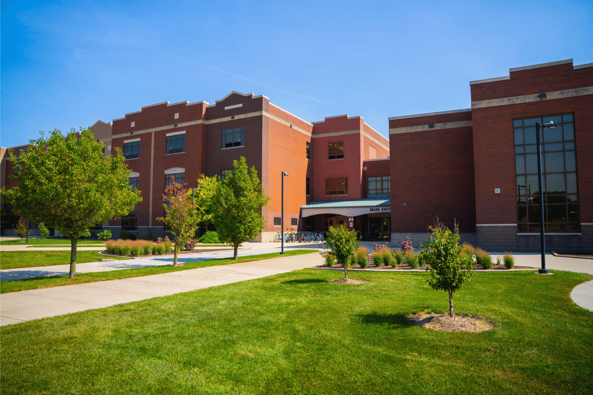 A sunny day view of a red brick school building with a green lawn and trees in front.